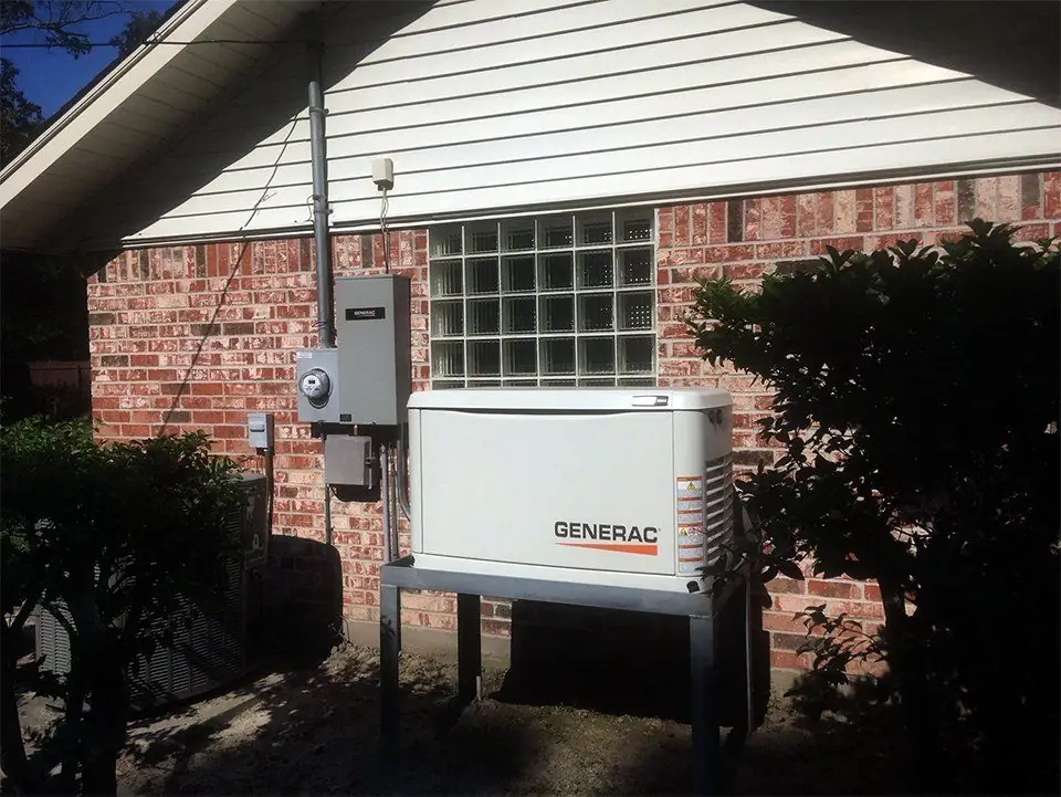 Generac standby generator installed on a concrete pad against the brick exterior of a house